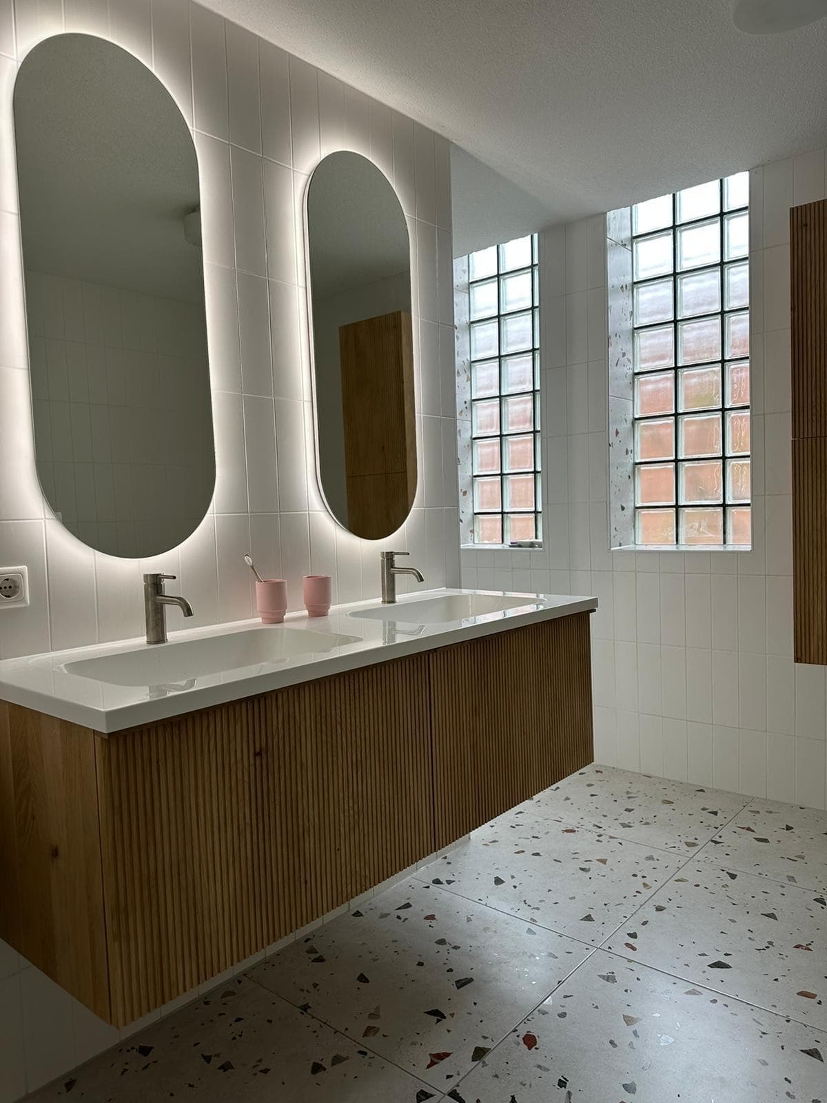 Badkamer met dubbele wastafel, twee ovale spiegels met verlichting en een houten meubel