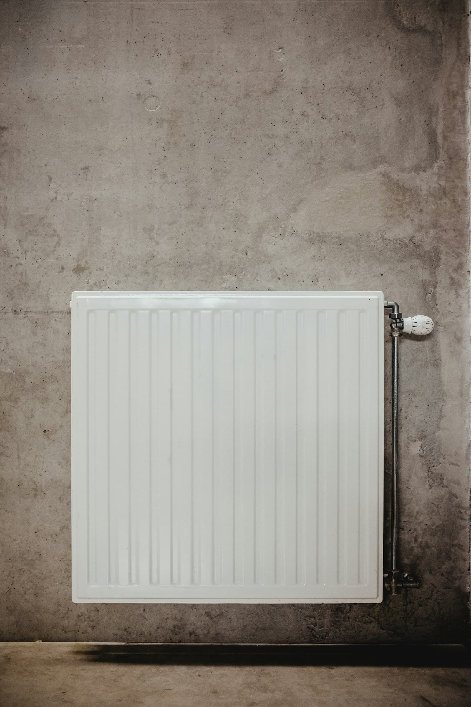 Wit paneelradiator tegen een betonnen wand