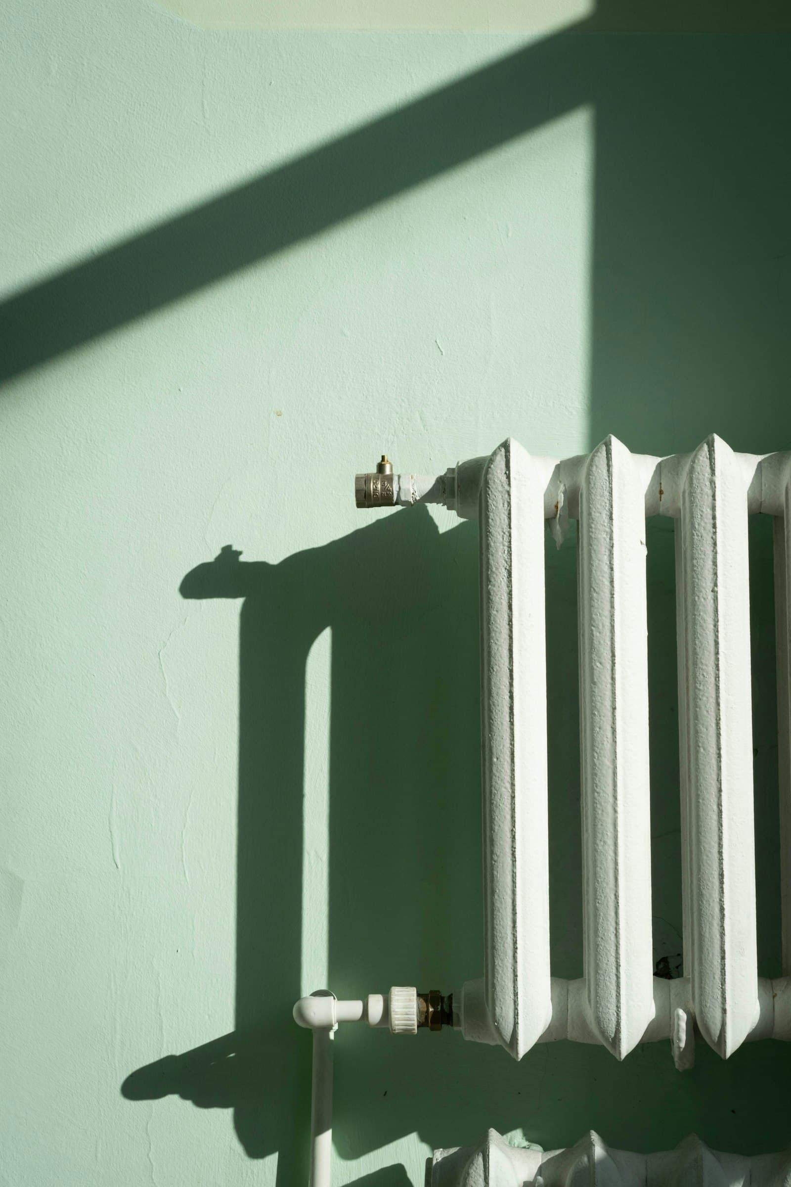 Witte radiator tegen een lichtgroene muur in de zon